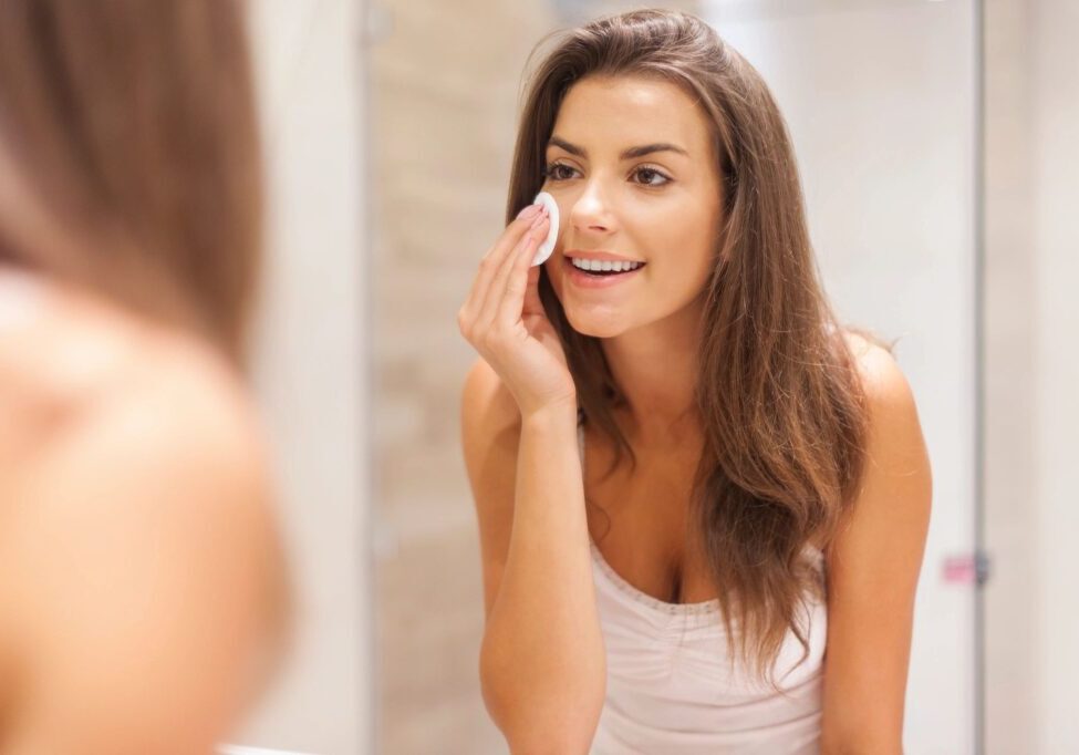 A woman is looking in the mirror and putting makeup on her face.